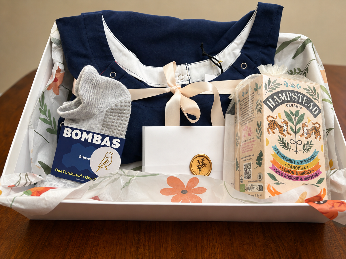 RN-designed Navy Comfort & Care Package featuring a soft organic cotton patient gown, Bombas gripper socks, organic tea, thoughtfully and individually wrapped with care in a high-end rigid gift box with free U.S. shipping and a complimentary handwritten card.