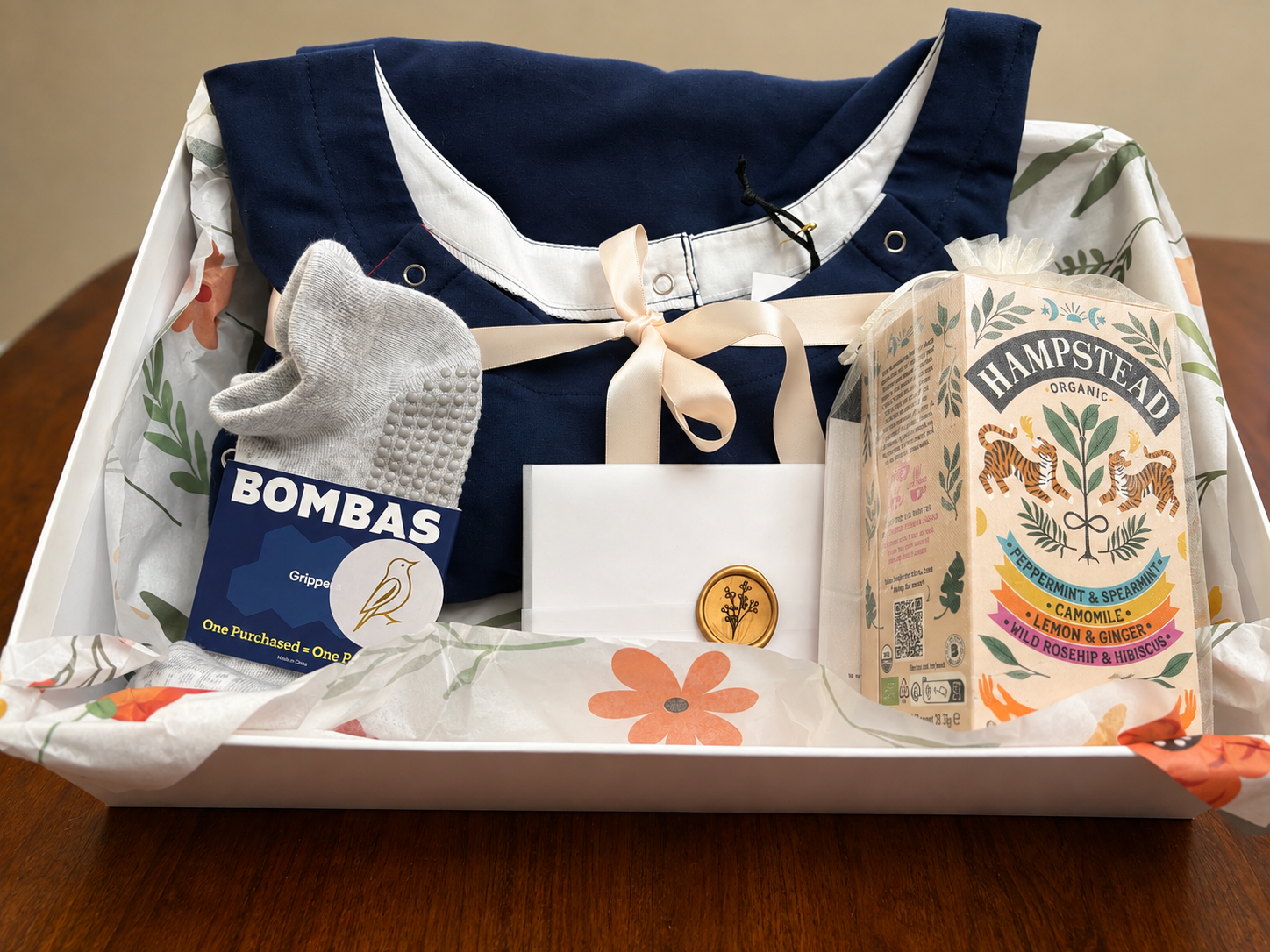 RN-designed Navy Comfort & Care Package featuring a soft organic cotton patient gown, Bombas gripper socks, organic tea, thoughtfully and individually wrapped with care in a high-end rigid gift box with free U.S. shipping and a complimentary handwritten card.