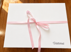A white rectangular gift box wrapped with a light pink ribbon showing how our Untethered gift sets are packaged 
