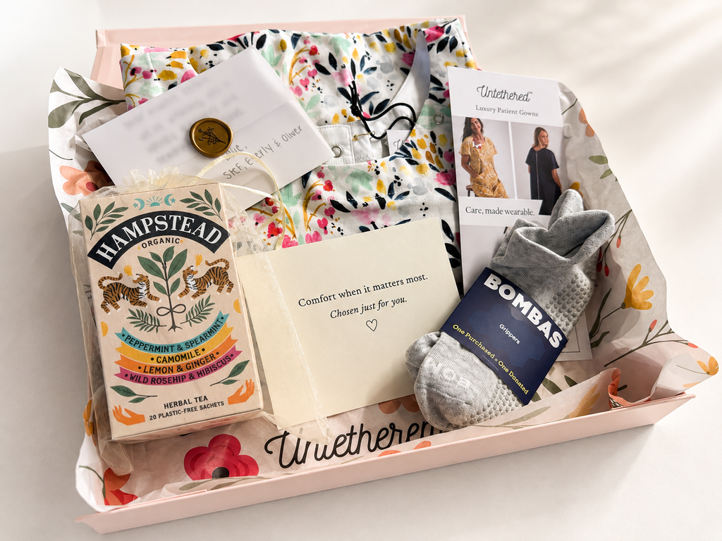 A curated gift box set from Unwetheren featuring a box of Hampstead herbal tea, grey knit socks by Bombas, a card from Unwetheren, our organic Two Hearts floral cotton patient gown, all thoughtfully displayed in a luxury gift box. 