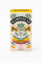 A box of Hampstead Organic herbal tea, Peppermint and Spearmint, Camomile, Lemon & Ginger, and Wild Rosehip & Hibiscus. The packaging features a cream-colored background with a yellow top, black brand lettering, and colorful illustrations of two tigers, green leaves, and ribbon banners. Box is included in our Comfort and Care Packages.